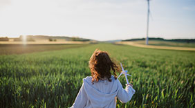 photo : Rear view of little girl standing in field with model of wind turbine. Concept of ecology future and renewable resources.